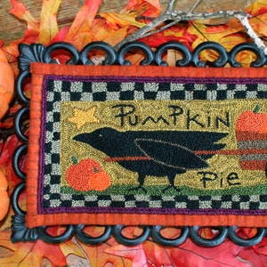 May include: A decorative fall-themed sign with the words "Pumpkin Pie" and a crow pulling a cart of pumpkins. The sign is framed in black and surrounded by orange pumpkins and fall leaves.