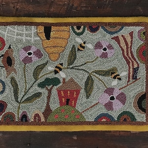 May include: A hand-stitched rug with a whimsical design featuring a beehive, bees, flowers, and a small house. The rug is made with a variety of colorful yarns and has a light green background.