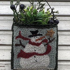 May include: A green felt wall hanging with a snowman holding a star. The snowman is wearing a red scarf and a black hat. The hanging is in a black metal frame with green foliage.