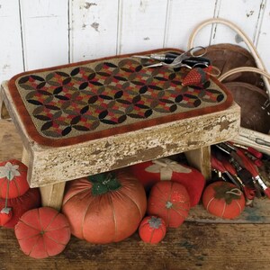May include: A wooden stool with a colorful patchwork cushion top. The stool is surrounded by several orange fabric pumpkins and a red fabric strawberry.