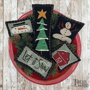 May include: Five small, hand-stitched felt ornaments in a red bowl. The ornaments are a snowman, a Christmas tree, a barn, a snowman with a red scarf, and a green and white ornament that says "Let it Snow".