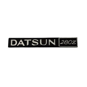 May include: Black and silver Datsun 280Z emblem. The emblem is rectangular and has a raised silver Datsun lettering and a silver 280Z in a square.