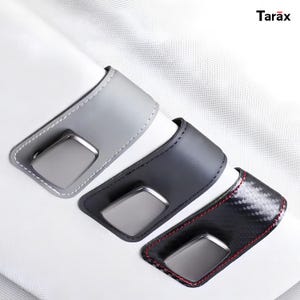 May include: Three automotive interior door handle covers with the brand name Tarax visible. The covers are light gray, dark gray, and a black carbon fiber pattern with red stitching. Each piece features a rectangular cutout for the handle.