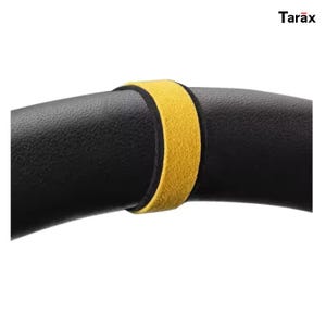 Könnte beinhalten: Ein schwarzer Lenkradbezug mit strukturierter Oberfläche und einem leuchtend gelben Mittelmarkierungsstreifen. Der Markenname Tarax ist in schwarzer Schrift in der oberen rechten Ecke aufgedruckt. Das Design hat eine gebogene, kreisförmige Form.