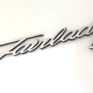 May include: Silver Fairlady emblem with a black outline. The word "Fairlady" is written in a cursive script.