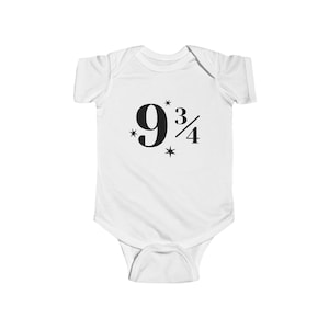 Peut inclure: Body bébé blanc avec le nombre "9 3/4" en noir, entouré de petites étoiles. Le body est un vêtement une pièce avec des manches courtes et une fermeture à boutons-pression en bas. Le motif est centré sur le devant.