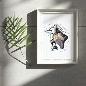 May include: A framed print with a black and white illustration of a person in a yoga pose. The background is a blue and gold watercolor design. The text "BE THE LIGHT YOU WISH TO SEE IN THE WORLD BE THE CHANGE YOU WANT TO SEE IN THE WORLD." is printed on the print.