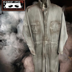 May include: A gray work jumpsuit with a button-up front and two chest pockets. The jumpsuit is slightly faded and has a distressed look. The text "Blackest Eyes FX" and "Custom Coverall Weathering" is visible on a label.
