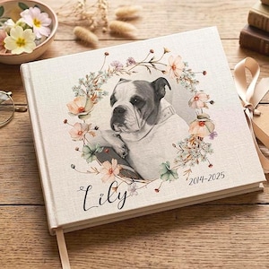Puede incluir: Un álbum de fotos de lino crema con un retrato de bulldog rodeado por una corona floral. La portada muestra el nombre "Lily" y los años "2014-2025". Se adjuntan una cinta crema y una etiqueta que dice "Handmade with Love".