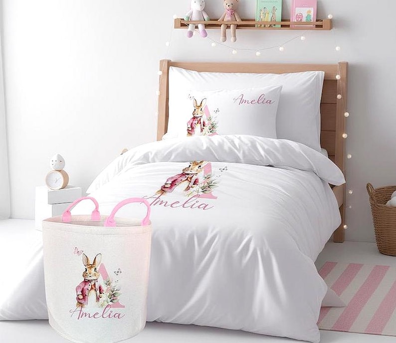 Personalised girls' bedding set featuring a classic watercolour pink bunny and a large floral-decorated initial 'E' for 'Emily'. The design is printed in soft pastel pinks and greens on a crisp white microfiber duvet cover.