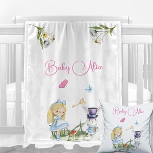 K&ouml;nnte beinhalten: Eine wei&szlig;e Babydecke mit einer Aquarell-Illustration von Alice im Wunderland-Charakteren, darunter Alice, der wei&szlig;e Hase und ein Schl&uuml;ssel. Die Decke tr&auml;gt den Text "Baby Alice" in rosa kursiver Schrift.