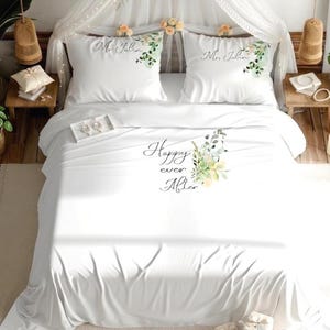 Peut inclure: Parure de lit blanche avec le texte "Happy ever After" et des motifs floraux. Deux taies d'oreiller blanches sont brodées des noms "Mr. John" et de motifs floraux. Le lit est décoré d'un baldaquin et de tables de chevet.