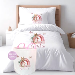 Juego de funda nórdica personalizada con diseño de conejo rosa en acuarela, ropa de cama con mariposas arcoíris y cesta de juguetes.