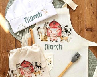 May include: A white chef's hat, apron, drawstring bag, and other kitchen tools are displayed on a wooden surface. The apron and bag feature a farm scene with a red barn, pig, horse, and cow. The name "Diamh" is printed on the hat, apron, and bag.