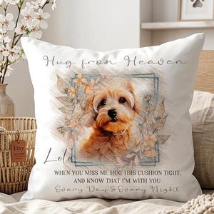 May include: A white square throw pillow featuring a sketch-style illustration of a small tan dog centered within a blue rectangular frame. The text reads Hug from Heaven, Lola, and When you miss me hug this cushion tight, and know that I'm with you every day & every night.