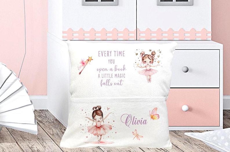 Op de afbeelding: Wit kussen met een zak, met illustraties van een ballerina, een toverstaf en vlinders. De tekst luidt: "Elke keer als je een boek opent, valt er een beetje magie uit." De naam "Olivia" wordt ook weergegeven.