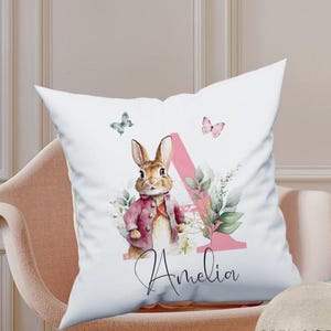 Close-up of the matching personalised pillow showing the delicate watercolour rabbit and floral alphabet art. The print is soft-touch and integrated into the fabric for comfort during sleep.