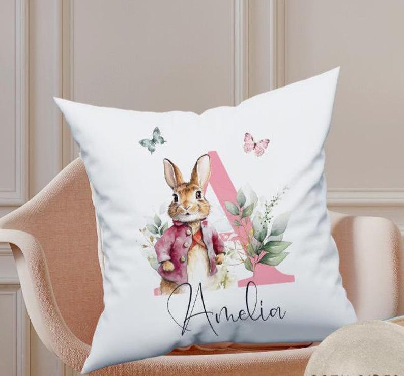 Close-up of the matching personalised pillow showing the delicate watercolour rabbit and floral alphabet art. The print is soft-touch and integrated into the fabric for comfort during sleep.