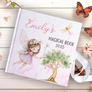 Może przedstawiać: Twarda oprawa książki z różowym marmurowym wzorem, z ilustracją wróżki i tekstem "Emily's MAGICAL BOOK 2025". Okładka zawiera wróżkę ze skrzydłami, drzewo i ważkę. Dołączona jest biała wstążka.