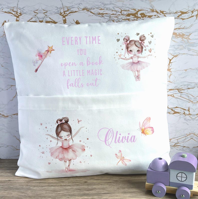 Op de afbeelding: Wit kussen met een zak, met illustraties van ballerina's, vlinders en een toverstaf. De tekst luidt "Every time you open a book a little magic falls out" en de naam "Olivia".