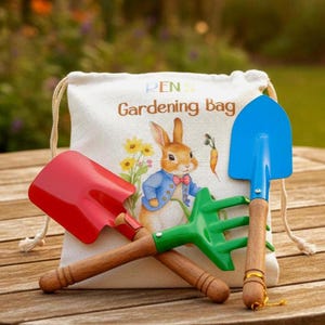 May include: A children's gardening set with a canvas bag featuring a rabbit illustration. The set includes a red shovel, a green rake, and a blue trowel, all with wooden handles. The bag reads "Gardening Bag".