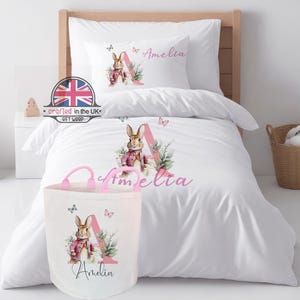 A coordinated pink bunny nursery set featuring the personalised duvet cover alongside a matching 50L canvas laundry and toy storage basket. Both feature the floral 'E' initial for a cohesive bedroom theme.