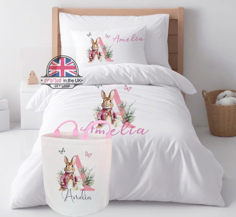 A coordinated pink bunny nursery set featuring the personalised duvet cover alongside a matching 50L canvas laundry and toy storage basket. Both feature the floral 'E' initial for a cohesive bedroom theme.