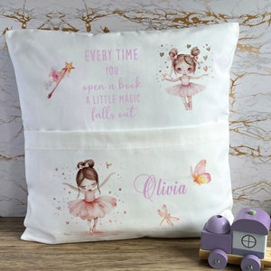 Op de afbeelding: Wit kussen met een zak, versierd met illustraties van ballerina's in roze tutu's, een toverstaf, vlinders en de naam "Olivia". De tekst luidt: "Elke keer als je een boek opent, valt er een beetje magie uit."