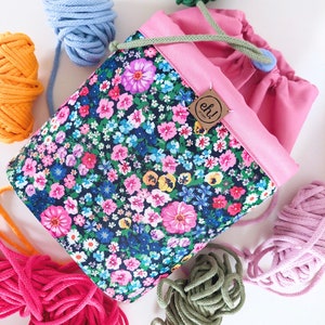 Pode incluir: Uma bolsa de projeto com cord&atilde;o e estampa floral com interior e acabamento rosa. A bolsa &eacute; cercada por meadas de fios coloridos em azul, laranja, rosa, verde e roxo. Uma pequena etiqueta com o texto "eh! project" est&aacute; anexada.