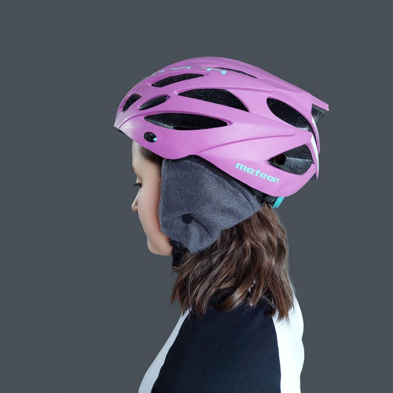 K&ouml;nnte beinhalten: Ein pinkfarbener Fahrradhelm mit dem Wort "meteor" auf der Seite. Der Helm hat mehrere Bel&uuml;ftungs&ouml;ffnungen und wird mit einem grauen Ohrenw&auml;rmer getragen. Die Person tr&auml;gt ein schwarz-wei&szlig;es Oberteil.