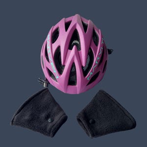K&ouml;nnte beinhalten: Ein magenta Fahrradhelm mit dem Wort "MARVET" in t&uuml;rkisfarbenen Buchstaben. Der Helm hat mehrere Bel&uuml;ftungs&ouml;ffnungen und ein schwarzes Innenfutter. Zwei schwarze Ohrensch&uuml;tzer mit Druckkn&ouml;pfen sind enthalten.