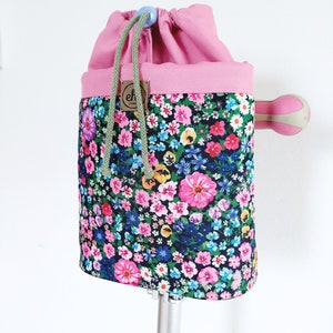 Pode incluir: Uma bolsa com cord&atilde;o floral com uma parte superior rosa e um cord&atilde;o verde. A bolsa apresenta um padr&atilde;o floral colorido com flores rosa, azuis, amarelas e brancas sobre um fundo escuro. Uma pequena etiqueta castanha com as letras "eh" est&aacute; anexada.