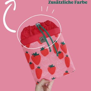 Pode incluir: Uma bolsa com cord&atilde;o com a parte superior vermelha e o corpo rosa. O corpo da bolsa &eacute; estampado com morangos vermelhos. O cord&atilde;o &eacute; verde. O texto "Additional color" est&aacute; no topo.