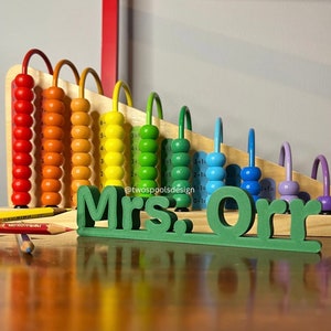 May include: A wooden abacus with colorful beads and a green wooden sign that reads "Mrs. Orr".
