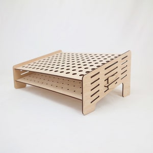 Può includere: Un supporto in legno a due livelli con un motivo a griglia e fori per contenere oggetti. Il supporto è in legno marrone chiaro e ha un design moderno.