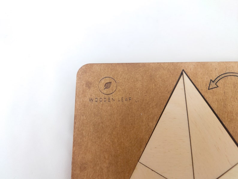 May include: A wooden geometric puzzle with a pyramid shape. The puzzle is made of light wood and has a brown wooden base with the logo "Wooden Leaf" printed on it.