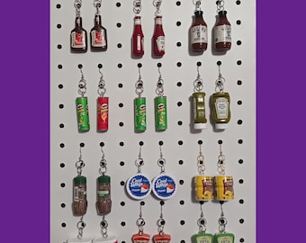 May include: A collection of miniature food earrings, including bottles of ketchup, mustard, hot sauce, and other condiments, as well as chips, cheese, and other snacks.