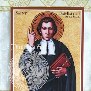 May include: A religious icon of Saint Jean-Baptiste de La Salle, a Catholic priest and educator. The icon is painted in a traditional style with a gold background and a halo around the saint's head. He is depicted wearing a black cassock and a white collar, holding a book in his left hand and gesturing with his right hand. The icon is framed in a brown wooden frame.