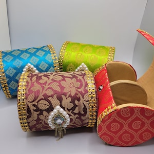 May include: Four decorative, cylindrical containers in teal, lime green, burgundy, and red. Each is trimmed with gold and embellished with pearls and jewels. The burgundy container has a heart-shaped jewel pendant.