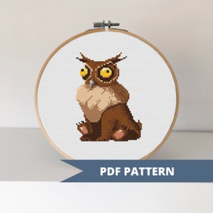 May include: Cross stitch pattern of a brown owl with large yellow eyes. The owl is sitting on a white background. The pattern is in a hoop and says "PDF PATTERN" below it.