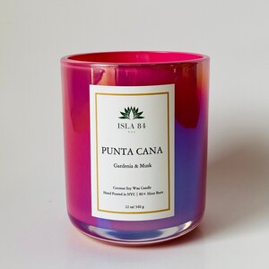 K&ouml;nnte beinhalten: Ein leuchtender, irisierender Glas-Kerzenhalter mit einem rosa-violetten Farbverlauf. Das Etikett tr&auml;gt die Aufschrift "PUNTA CANA" und "Gardenia & Musk". Es ist eine 340 g Kerze, handgegossen in NYC, mit einer Brenndauer von 80+ Stunden.