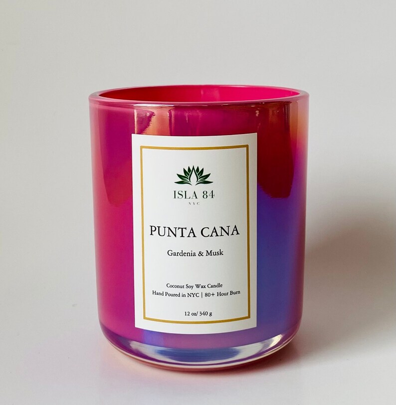 K&ouml;nnte beinhalten: Ein leuchtender, irisierender Glas-Kerzenhalter mit einem rosa-violetten Farbverlauf. Das Etikett tr&auml;gt die Aufschrift "PUNTA CANA" und "Gardenia & Musk". Es ist eine 340 g Kerze, handgegossen in NYC, mit einer Brenndauer von 80+ Stunden.