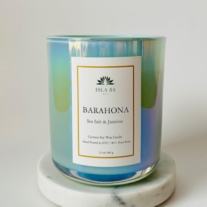 Puede incluir: Un tarro de vela de vidrio iridiscente azul verdoso con una etiqueta blanca que dice "ISLA 84 NYC" y "BARAHONA Sea Salt & Jasmine". La etiqueta tambi&eacute;n incluye el texto "Coconut Soy Wax Candle", "Hand Poured in NYC", "80+ Hour Burn", y "12 oz/340 g".