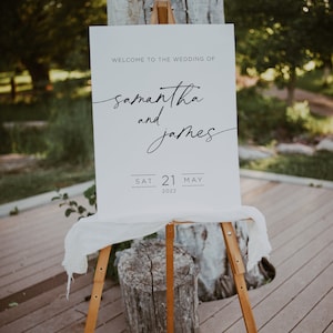 May include: White wedding sign with black text announcing the wedding of Samantha and James on Saturday, May 21, 2022.