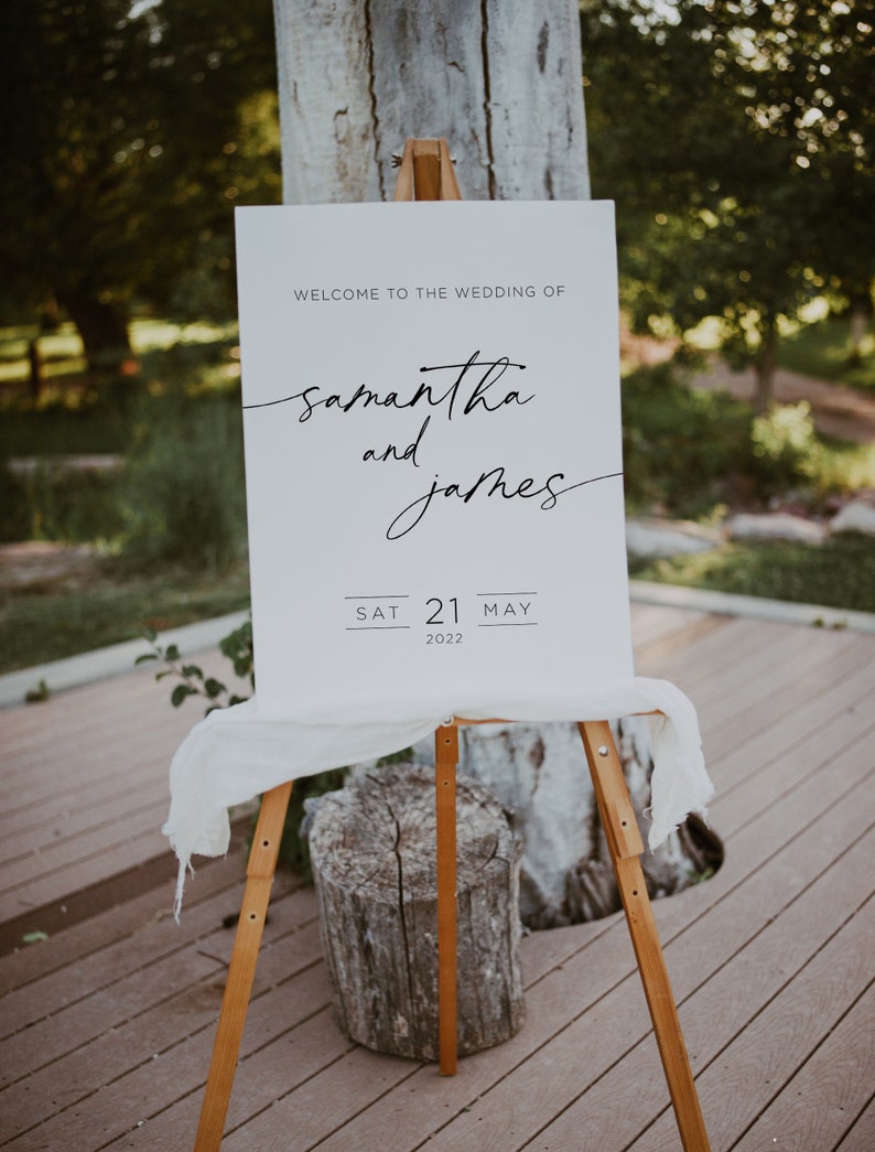 May include: White wedding sign with black text announcing the wedding of Samantha and James on Saturday, May 21, 2022.