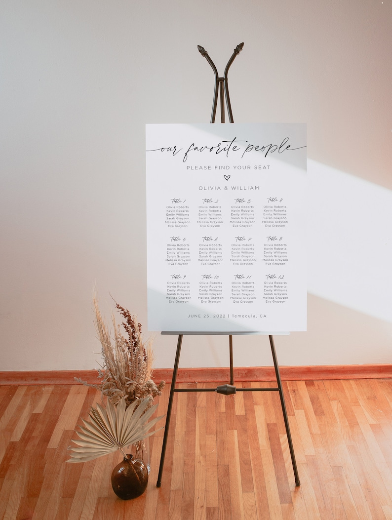 May include: A white seating chart with the text "our favorite people" and "PLEASE FIND YOUR SEAT" at the top. Below the text is a heart symbol and the names "OLIVIA & WILLIAM". The chart lists the names of guests assigned to each table number, from Table 1 to Table 12. The date "JUNE 25, 2022" and location "Temecula, CA" are printed at the bottom of the chart.