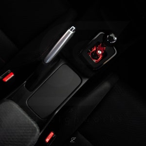 Peut inclure: Gros plan sur l'int&eacute;rieur d'une voiture, montrant un si&egrave;ge en cuir noir, un levier de frein &agrave; main argent&eacute; et un pommeau de levier de vitesse rouge apr&egrave;s-vente.