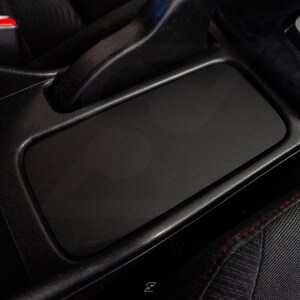 Peut inclure: Int&eacute;rieur de voiture noir avec une console centrale en cuir noir et un accoudoir &agrave; surpiq&ucirc;res rouges.