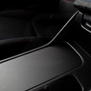 Peut inclure: Int&eacute;rieur de voiture noir avec une console centrale en cuir noir et des surpiq&ucirc;res rouges. La console a un compartiment de rangement avec un couvercle noir.
