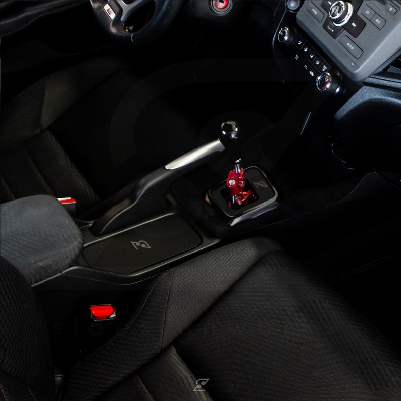 Peut inclure: Int&eacute;rieur de voiture noir avec un pommeau de levier de vitesse rouge et argent. La voiture a des si&egrave;ges en cuir noir et un tableau de bord noir. Le pommeau de levier de vitesse est situ&eacute; dans la console centrale.